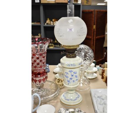 A Victorian opaque glass oil lamp, the body hand painted with stylised blue flowers and heightened with gilding, having a sph