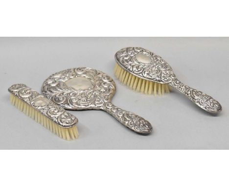 An Elizabeth II hallmarked silver three piece dressing table set with elaborate scroll embossed detail, Birmingham 1956, leng