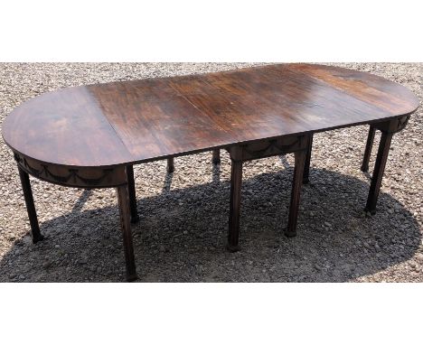 An Edwardian mahogany dinning room table formed of two demi-lune table and a central gate leg table, with swag and vine leaf 