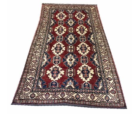 KAZAK RUG, 214cm x 122cm, rows of geometric medallions on a deep ruby field within corresponding borders.
