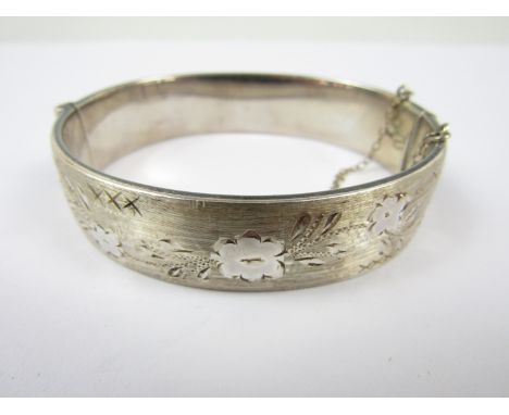 A mid 20th Century silver hinged bangle, the face engraved with a running floral design