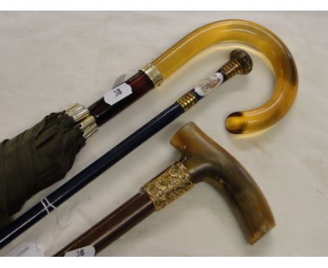 A porcelain handled umbrella, a horn handled walking stick and another umbrella, (3).