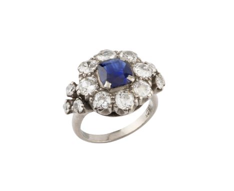 A sapphire and diamond cluster ring, the cushion-shaped mixed-cut sapphire claw set within an old-cut diamond border, between