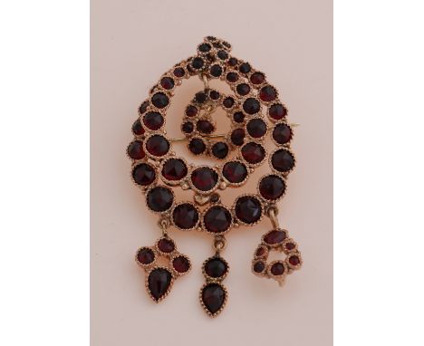 Yellow gold brooch, 585/000, with garnet. Oval-contoured brooch with pendants, completely set with garnet stones, some slight