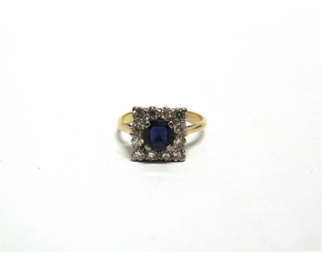 A SAPPHIRE AND DIAMOND CLUSTER RING stamped '18ct', the square cut stone enclosed by twelve single cut diamonds, finger size 