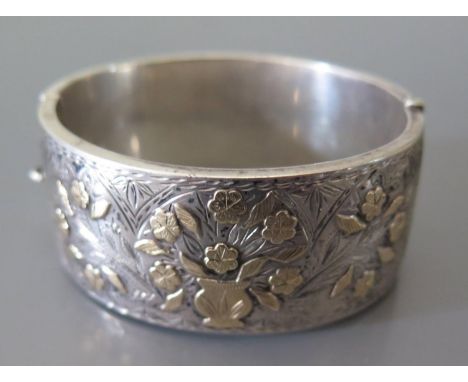 A Silver and Gold Mounted Hinged Bangle with raised and chased floral decoration 