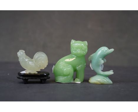 A collection of three oriental carved jade animals to include a cat, dolphin and a cockerel on wooden plinth. 