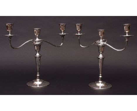 Two Elizabeth II three-light candelabra, each with urn shaped sconces on scrolling reeded arms to a central light with screw 