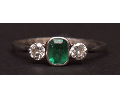 Mid-20th century precious metal emerald and diamond three-stone ring, the bezel set rectangular emerald between two claw set 