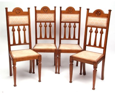 A set of four Arts & Crafts period light oak dining chairs with shaped backs featuring three stylised arrow designs to the ce