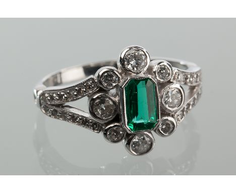 EMERALD AND DIAMOND CLUSTER RING
set with a central step cut emerald surrounded by brilliant cut diamonds, on diamond set spl