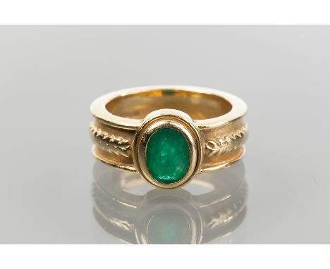 EMERALD RING
set with an oval cut emerald, on a wide band with ornate detailing to shoulders, in eighteen carat gold, 9.3g, s