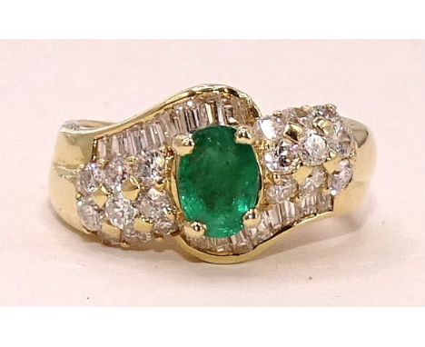 An emerald and diamond cluster ring claw-set an oval emerald between two lines of keystone and baguette-cut diamonds and two 