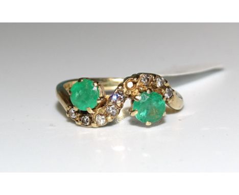 An emerald and diamond cross-over ring claw-set two round-cut emeralds and eight 8/8-cut diamonds, (one setting vacant), in 9