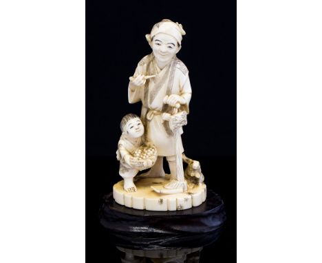 A Japanese ivory okimono of a farmer standing smoking a pipe, an infant with a basket of fruit and a hare, Meiji period 1868-