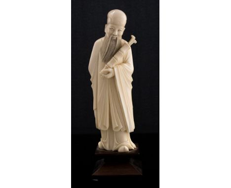 A 19th Century Chinese ivory tusk carving of a bearded elder, standing wearing a robe and holding an opium pipe tube, height 