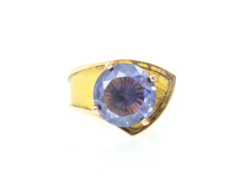 A synthetic alexandrite set dress ring, the round cut stone within a raised claw setting, upon yellow metal folded shank, sta