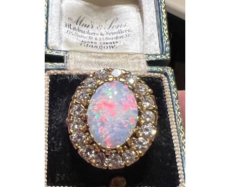 An opal and diamond cluster ring, the large precious opal oval cabochon claw set with a surround of seventeen transitional cu