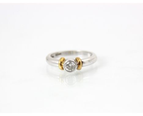 A platinum and diamond solitaire ring, the central round cut diamond within a rubover setting edge, with yellow metal spacers