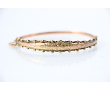 An early 20th century 9ct rose gold bangle, the raised engraved front with spherical and beaded detail to either side, with h