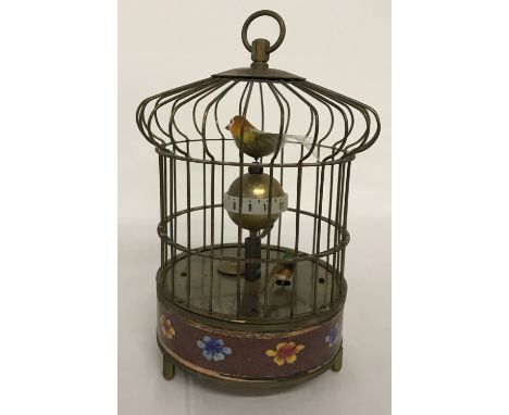 An ornamental wind up birdcage clock with cloisonné panel to base. The cage features two small feathered birds which rotate w
