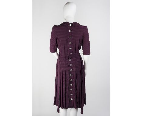 A maroon tea dress with flower detail to collared neckline, with short sleeves, pleated bodice and skirt with tie to waist an
