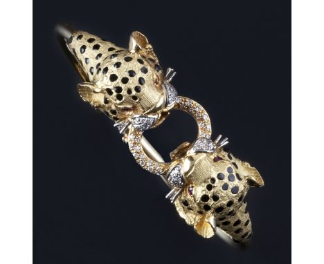 An enamel and gem set bangle, of hinged oval form, modelled as two leopard's heads, each with black spotted enamel decoration