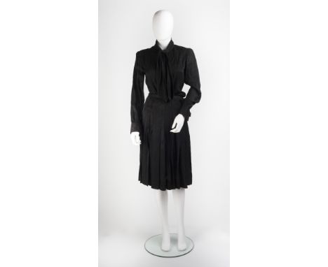 A black Yves Saint Laurent skirt and blouse set, the blouse with full length cuffed sleeves, buttons to front, and bow tie to