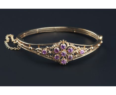 A 9ct gold and gem set bangle, of hinged oval trifurcated form, applied with a gem set flowerhead cluster and beaded decorati
