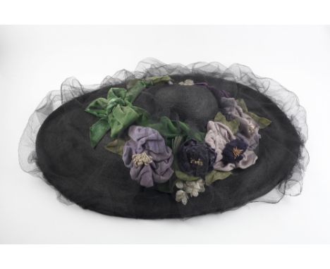 An Edwardian black straw hat, with velvet trim and mesh overlay, decorated with a wreath of violet, white and green flowerhea