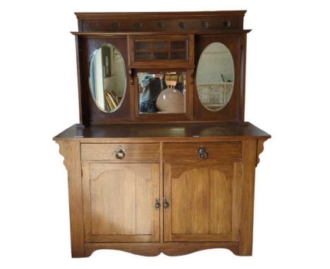 An oak Arts and Crafts style sideboard the mirrored back with heart pierced panel, small glazed central cupboard, the base fi