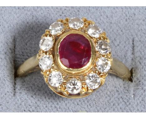 An 18 Carat Gold Ruby and Diamond Cluster Ring, an oval cut ruby in a rubbed over setting within a border of round brilliant 