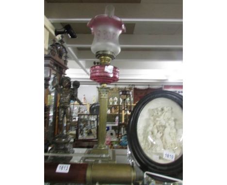 A brass Corinthian column oil lamp with cranberry glass font.