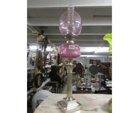 A silver plated Corinthian column oil lamp with cranberry glass font and shade.