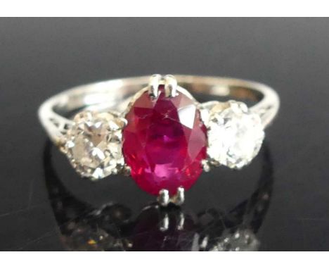 A white metal, ruby and diamond three-stone ring, featuring an oval cut ruby with a transitional brilliant cut diamond to eit