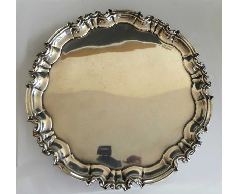 An Edwardian silver salver, of shaped circular form, having a piecrust rim and plain central ground, standing upon three scro