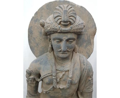 Ca.300AD. A substantial youthful and benign grey schist statue of the bodhisattva Avalokiteshvara on a plinth, seated wearing