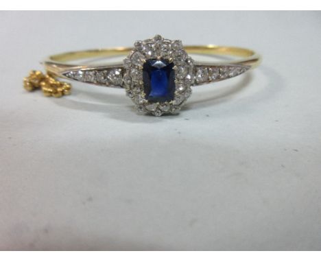 A sapphire and diamond hinged bangle, set to the front with a sapphire and diamond cluster comprising a cushion cut sapphire 