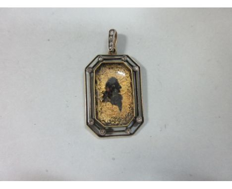 A gold leaf sillhouette and diamond set pendant, the octagonal glazed and closed back panel containing a black silhouette por