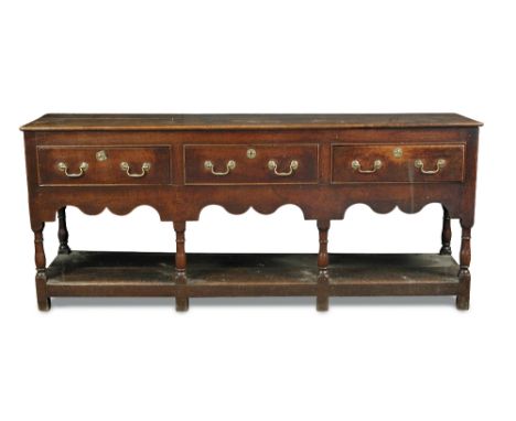 A George III oak dresser base, fitted three drawers with shaped apron, brass swan neck handles, open pot board base, on stile