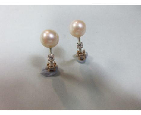 A pair of pearl and diamond earclips, each with a 9.5mm cultured pearl above a short knife-edge bar set with a round brillian