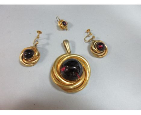 A garnet pendant and earring suite, each with a round cabochon garnet in a closed back collet within a loose knot-form nest o