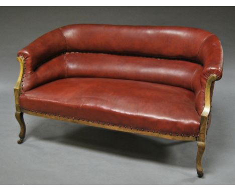 A button back red leather two seater sofa, early 20th century, raised on casters. 