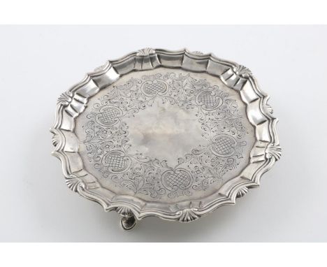 A GEORGE II WAITER. of shaped circular outline, with a husk and scroll border and chased foliate decoration, on three hoof fe