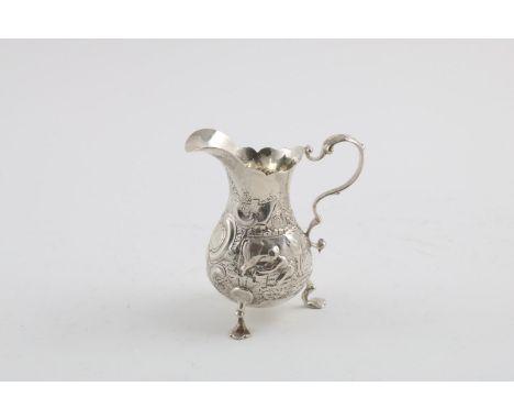 A VICTORIAN CREAM JUG. with a scroll handle, wavy rim and embossed with an agricultural landscape scene, on three feet, crest