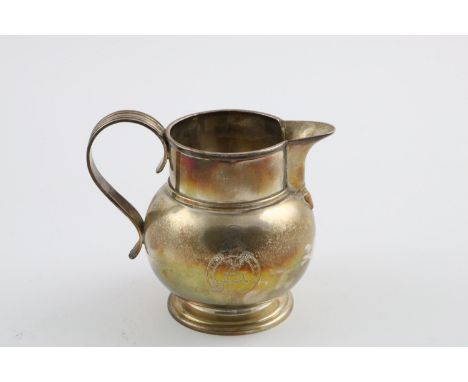 A GEORGE V MILK JUG. with a reeded loop handle, a squat round body and a circular foot, crested, by Pairpoint Brothers, Londo