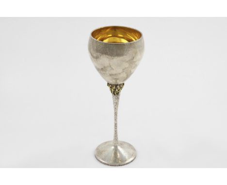 BY STUART DEVLIN:-. An Elizabeth II parcel-gilt goblet, with a textured stem with figures supporting the bowl and a hammered 