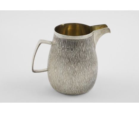 BY GERALD BENNEY:-. a modern milk jug, of tapering circular form with a textured finish and an angular handle, gilt interior,