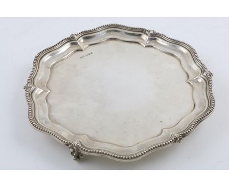 A GEORGE V SALVER. of shaped circular outline, with a bead border and raised on 3 ball and claw feet, by Walker &amp; Hall, S