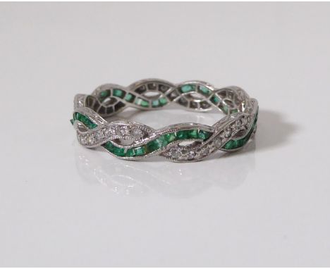 A mid-century Art Deco period platinum, emerald and diamond full eternity ring with two intertwining bands, one with 35 eight